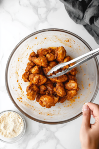 This image shows chicken pieces being coated evenly in cornstarch, preparing them for deep frying.