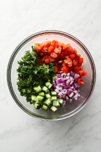 This image shows the process of whisking a dressing in a medium bowl, preparing to dress the fresh cucumber and tomato salad with a tangy, flavorful dressing.