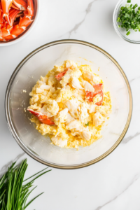 This image shows a handful of finely crushed cracker crumbs being sprinkled into the crab cake mixture, adding texture and helping to bind the ingredients together.