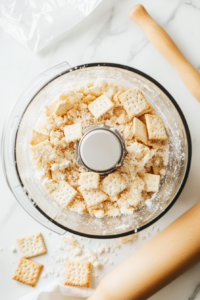 This image shows saltine crackers being crushed into fine crumbs in a bowl, creating a crispy coating for the fried crab legs that will add texture and crunch.