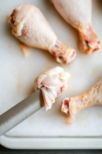 This image shows a knife cutting the tendons of a chicken leg to help form the signature lollipop shape.