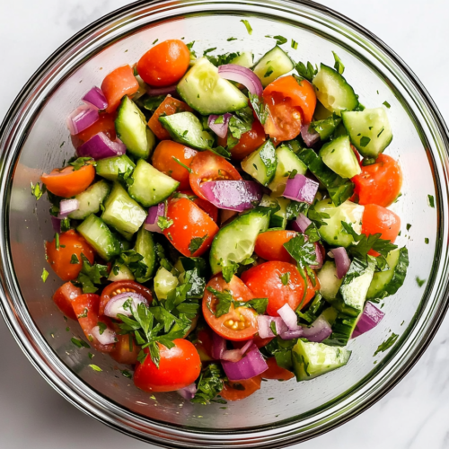 This image shows the process of combining freshly chopped cucumbers, tomatoes, onion, and parsley in a bowl, preparing the base for a refreshing cucumber and tomato salad.