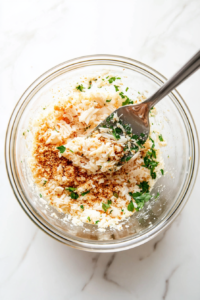 This image shows delicate lump crab meat being carefully folded into the mixture of breadcrumbs, seasonings, and wet ingredients to ensure even distribution without breaking the crab pieces.