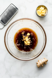 This image shows a glass bowl filled with soy sauce, ginger, garlic, and other seasonings being mixed together to create the Karaage marinade.