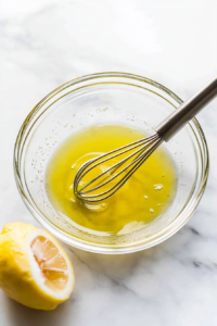 This image captures olive oil and freshly squeezed lemon juice being whisked together in a small bowl to create a flavorful marinade.