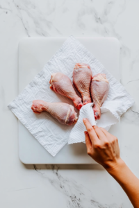 This image shows raw chicken legs being patted dry with a paper towel, ensuring better texture when cooked.