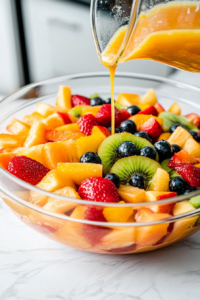 This image shows the cooled sauce being poured over the fresh fruit, ensuring an even coating to bring all the flavors together in the German Fruit Salad.