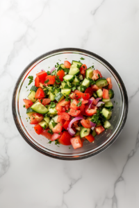 This image shows a vibrant cucumber and tomato salad featuring freshly chopped cucumbers, tomatoes, onions, and cilantro, creating a colorful and refreshing dish.