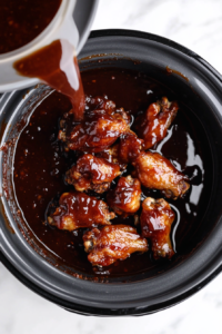 rich-honey-bbq-sauce-being-poured-over-chicken-wings-in-the-slow-cooker