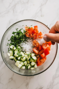 This image shows the process of pouring the dressing over the salad and tossing it to evenly coat the fresh cucumbers, tomatoes, onions, and parsley with the dressing.