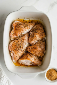 This image shows seasonings being generously sprinkled over the split chicken breast, adding depth of flavor and an aromatic touch before baking.