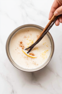 straining-infused-milk-mixture-to-remove-cinnamon-stick-vanilla-bean-and-lemon-zest