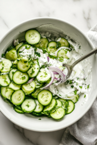 This image shows a bowl of sour cream being whisked with vinegar, dill, and seasonings, creating a smooth and tangy dressing for the German cucumber salad.