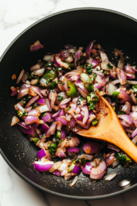 adding-green-chilies-and-onions-to-the-black-skillet-for-flavorful-curry-base