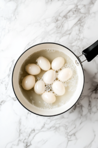 This image shows perfectly boiled eggs that have been peeled and sliced in half lengthwise, neatly arranged on a white round plate, ready for the egg puff filling.